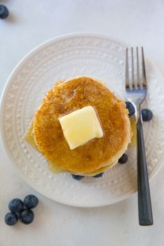 a white plate topped with pancakes covered in butter and blueberries next to a fork