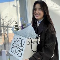 a woman is holding a bag and flowers in front of a window with the words love written on it