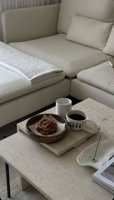 a table with a plate of food and two cups of coffee on it next to a couch