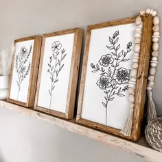 three framed art pieces on a mantle in a living room, one with flowers and the other with feathers