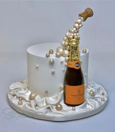 a cake with a bottle of champagne and pearls on the top is decorated in white icing