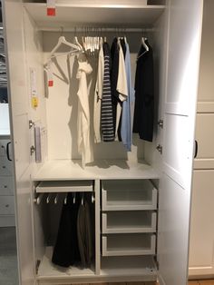 an organized closet with clothes hanging on hooks and drawers, including shirts and pants in white cabinets