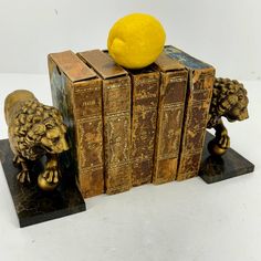 an orange sitting on top of two books with lions figurines next to it