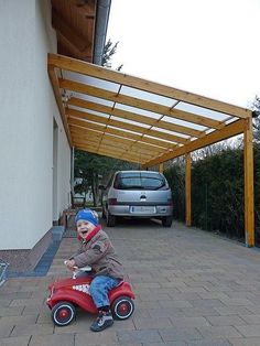 a little boy riding a toy car in front of a building with a carport