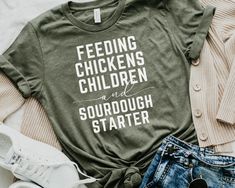 Celebrate your love for sourdough, chickens and your children with this cozy t-shirt, perfect for homestead mamas and chicken lovers. This funny and faith-inspired tee makes an ideal Mother's Day gift for any bread-baking enthusiast or homeschool mama. HOW TO ORDER - Visit photos for sizing and measurements - Select size and color from dropdown menu - Add customization to box if required - Add to cart & proceed to checkout * If you are ordering multiple, then go back to listing and perform steps Farm Wardrobe, Sourdough Shirt, Wardrobe Makeover, Chicken Shirts, Mommy Style, Chicken Lovers, Vinyl Shirts, Sourdough Starter, T Shirt Funny