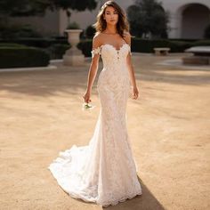 a woman in a white wedding dress standing on a dirt road with her hand on her hip