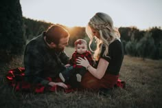 a man and woman sitting on the ground with a baby in their lap looking at each other