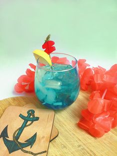 a wooden tray topped with a glass filled with blue liquid and an anchor cutout