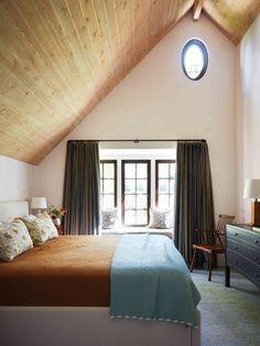 a large bed sitting under a window in a bedroom next to a dresser and chair