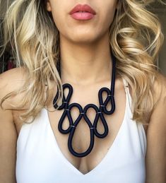 a woman with blonde hair wearing a white tank top and black necklace on her neck