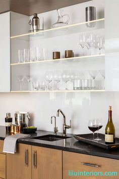 a kitchen counter with wine glasses and bottles on the shelves above it, next to a sink