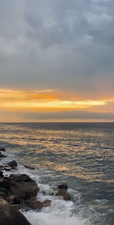 the sun is setting over the ocean and rocks