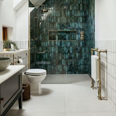 a bathroom with a toilet, sink and shower in it's center wall that has green tiles on the walls