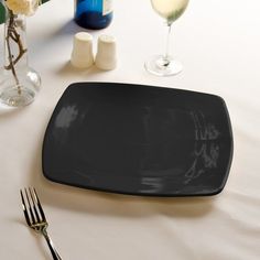 a black plate sitting on top of a table next to two wine glasses and flowers