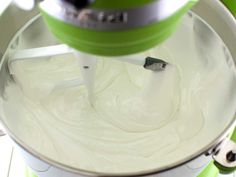 a mixer is mixing white cream in a green bowl