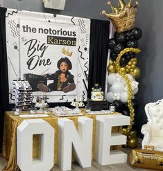 a table with balloons and decorations for a one year old birthday party in gold, black and white