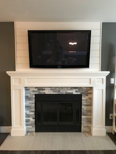 a flat screen tv mounted on the wall above a fireplace in a room with gray walls