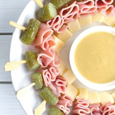 a white plate topped with meat and veggies next to a bowl of dip