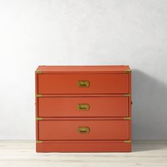 an orange chest of drawers with gold handles on a white floor next to a gray wall