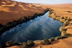 an aerial view of a lake surrounded by sand dunes and palm trees in the desert