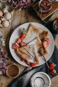 pancakes with strawberries and powdered sugar sit on a plate next to cups of coffee