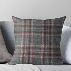 a gray and red plaid pillow sitting on top of a couch next to two pillows