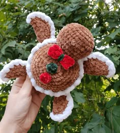 a hand holding up a brown and white stuffed animal with red flowers on it's head