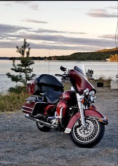 a red motorcycle parked on top of a gravel road next to the ocean and trees