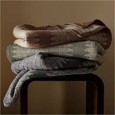 three folded blankets stacked on top of each other in front of a brown wall and chair