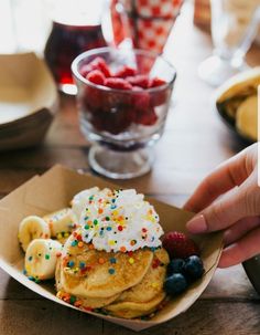 a person is reaching for some fruit on top of pancakes with whipped cream and sprinkles