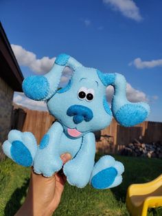 a hand holding a blue stuffed dog in front of a yellow plastic chair and green grass