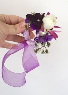 a hand holding a purple and white boutonniere with flowers on it's side