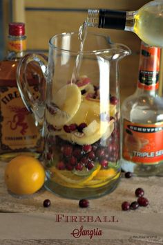 a pitcher filled with lemons and cranberries being poured into the pitcher to make punch