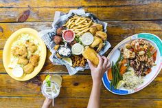 two plates of food on a wooden table with people holding their hands over the plate