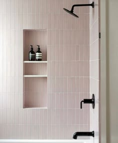 a white bath tub sitting next to a shower with black fixtures on the wall and shelves above it