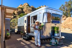 a woman in white overalls standing next to a silver trailer with flowers on it