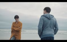 two people standing on the beach looking at something