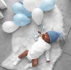 a baby is laying on a white rug with blue and white balloons in the background