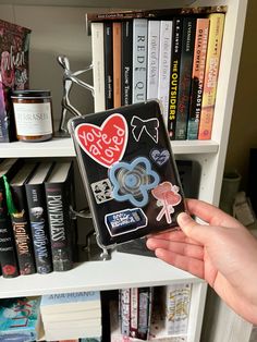 someone is holding up some stickers in front of a book shelf full of books