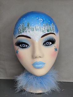 a mannequin's head is decorated with blue and white makeup, furs and snow