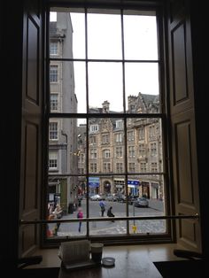 an open window looking out onto a street with people walking on it and buildings in the background