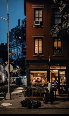 people are walking past a small restaurant on the side of the street at night time