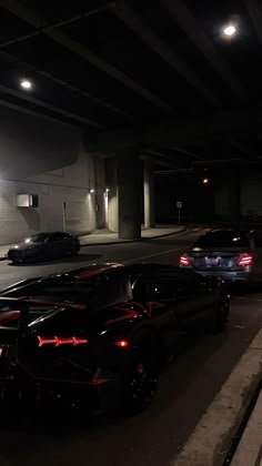 some very nice looking cars parked in a parking lot at night with the lights on