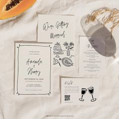 the wedding stationery is laid out on top of white paper with black ink and an orange slice next to it