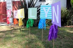 colorful yard signs are displayed in front of a house with palm trees and bushes behind them