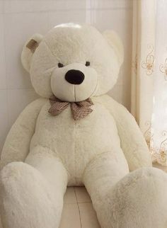 a large white teddy bear sitting on the floor next to a window with curtains behind it