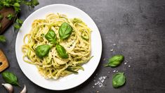 a plate of pasta with basil and parmesan cheese on a dark table top