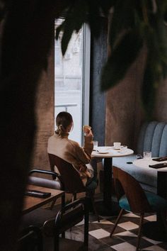 a woman sitting at a table with a cup in her hand and looking out the window