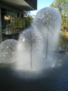 three umbrellas are spewing out of the water in front of a building