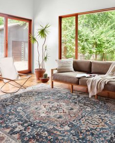 a living room with a couch, chair and rug on the floor in front of large windows